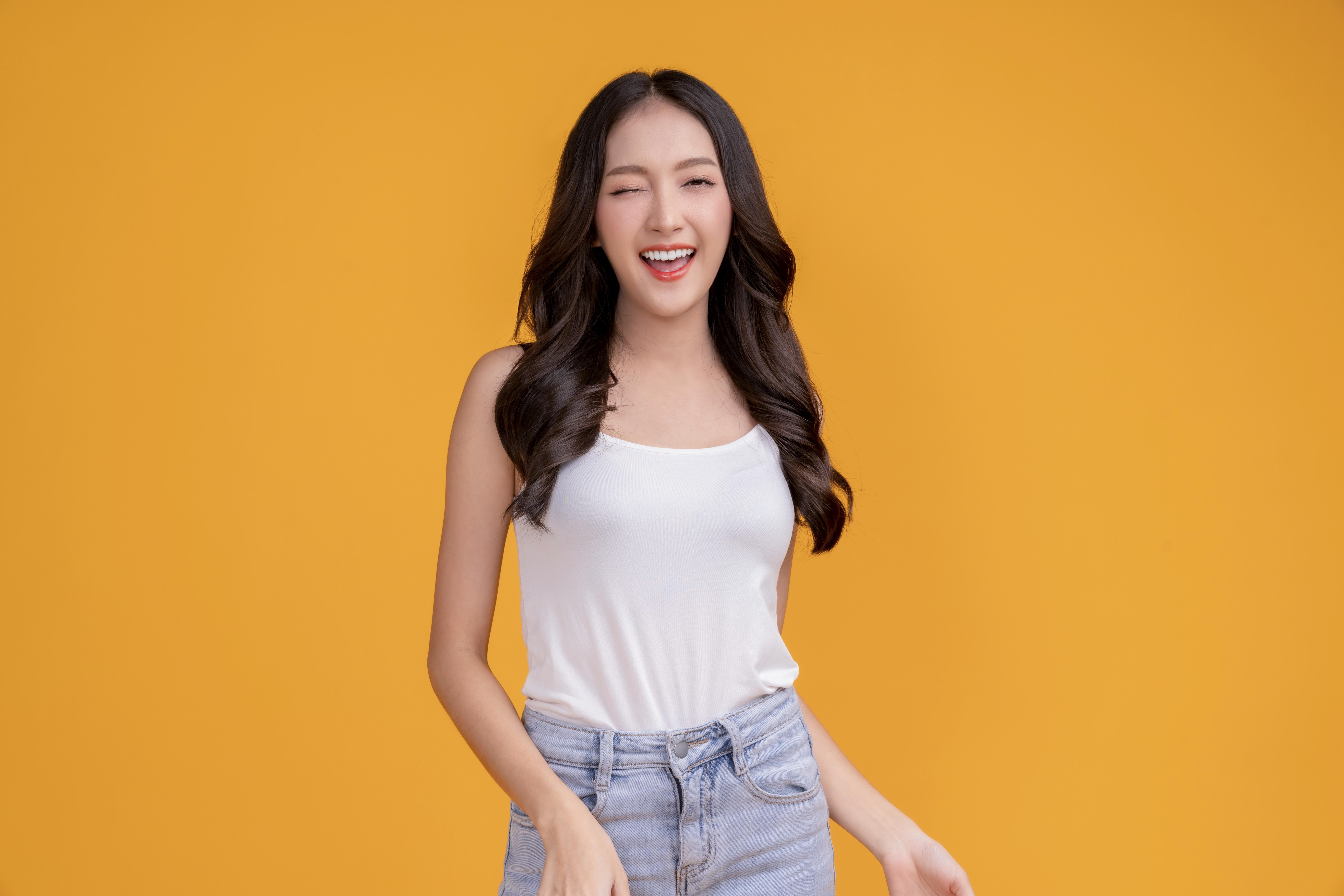 casual-happiness-asian-female-woman-smiling-cheerful-white-tshirt-blue-jean-relax-peaceful-positive-thinking-carefree-lifestyle-standing-with-yellow-color-background-studio-shoot